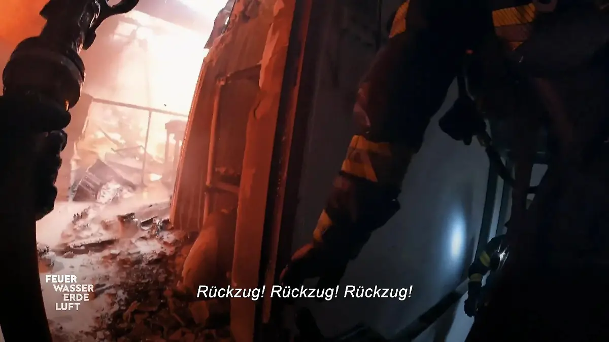Feuer, Wasser, Erde, Luft - Retter in ihrem Element: Brandsituation in einer zerstörten Lagerhalle. Schriftzug: „Rückzug! Rückzug! Rückzug!”