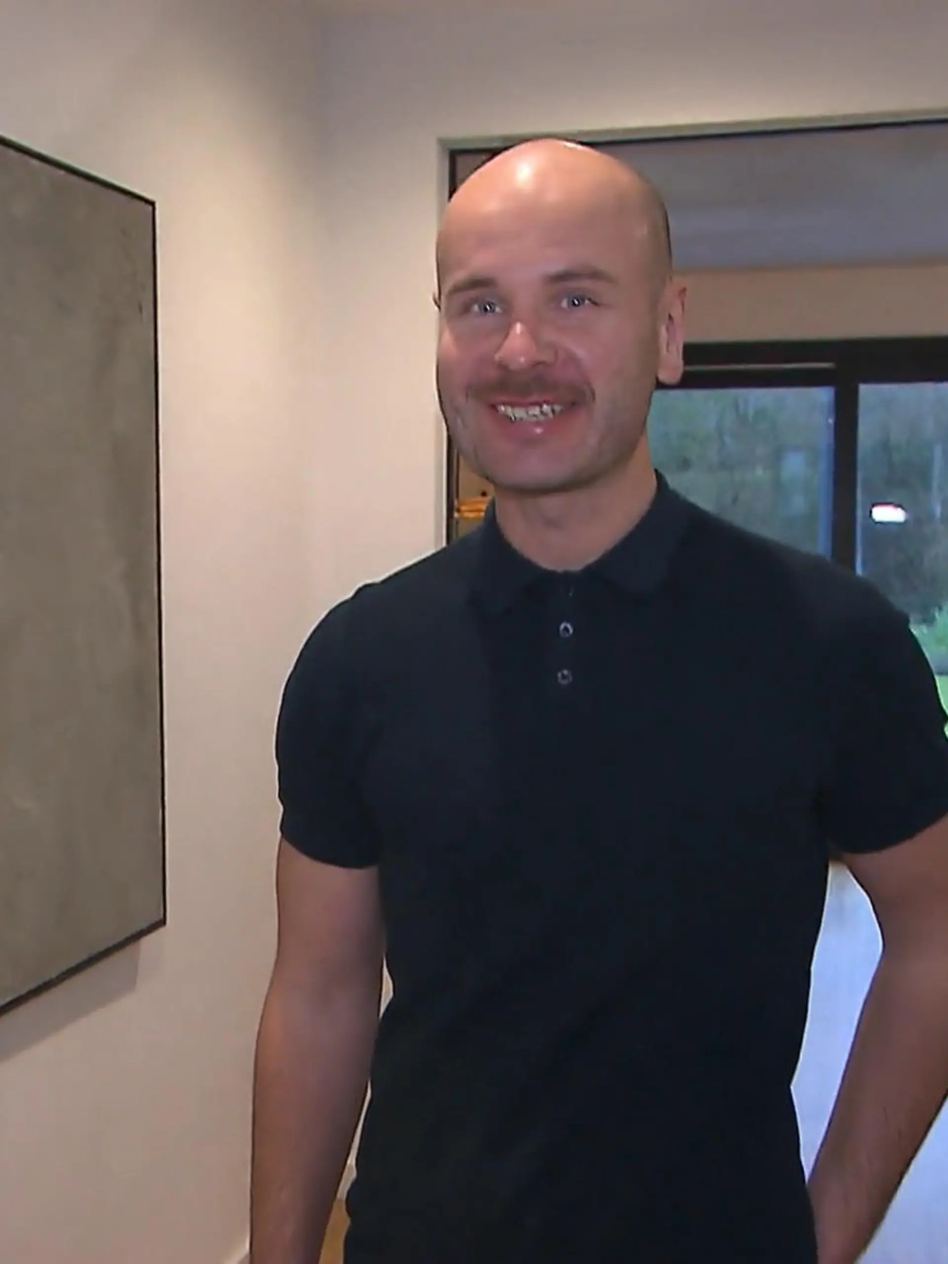 Das perfekte Dinner: Schlanker Mann mit Glatze und schwarzem Poloshirt im minimalistischen Flur seines Hauses