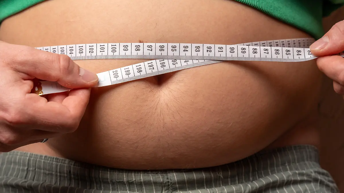 Ein Mann misst seinen Bauchumfang mit einem Maßband und zeigt Übergewicht sowie Adipositas. Das Bild steht für gesundheitliche Risiken und den Wunsch abzunehmen durch Ernährung, Bewegung und Veränderung des Lebensstils.