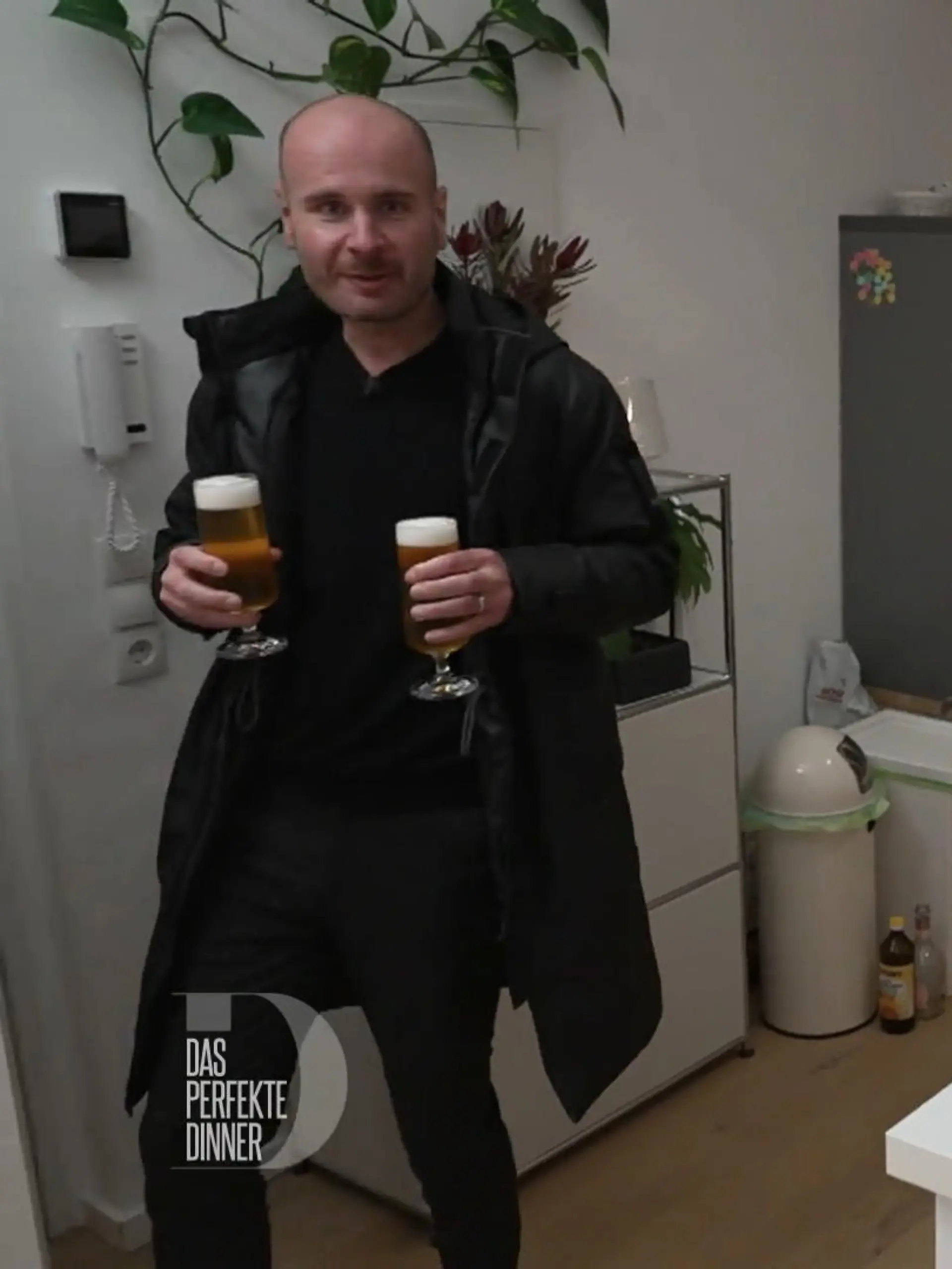 Das perfekte Dinner: Ein Gast steht in Jacke mit zwei frisch gezapften Gläsern Pils in der Hand an der Wohnungstür.