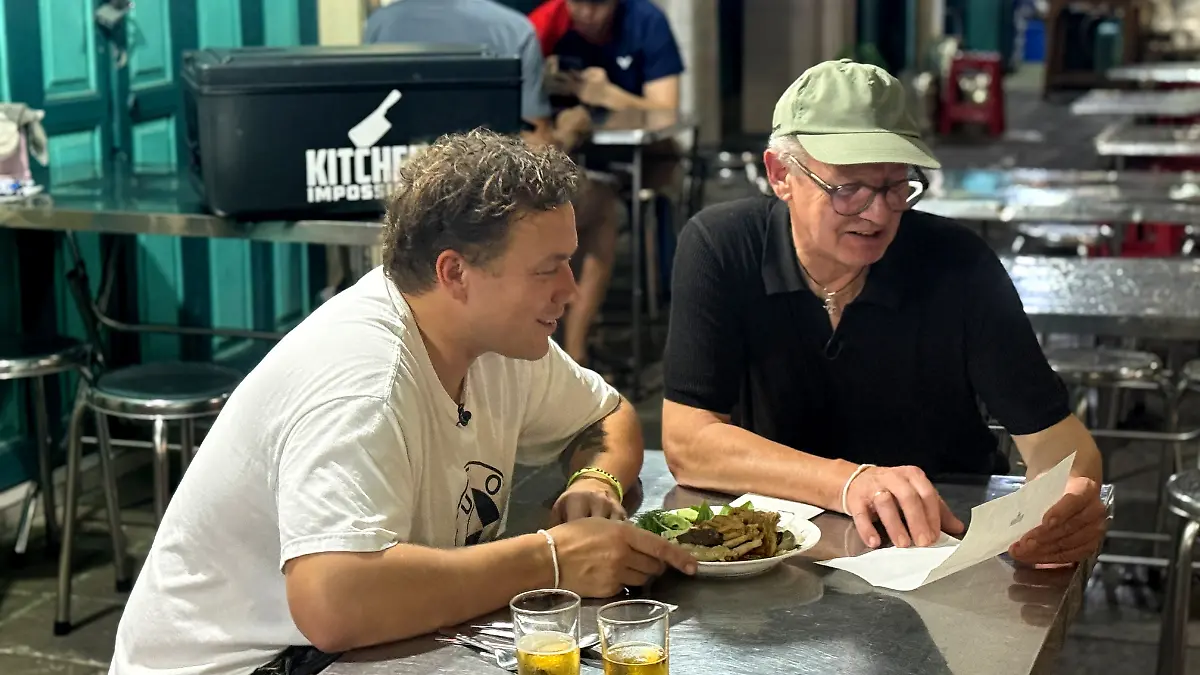 Kitchen Impossible: Helmut und Philip Rachinger sitzen in einer thailändischen Garküche vor einem Gericht und lesen eine Nachricht