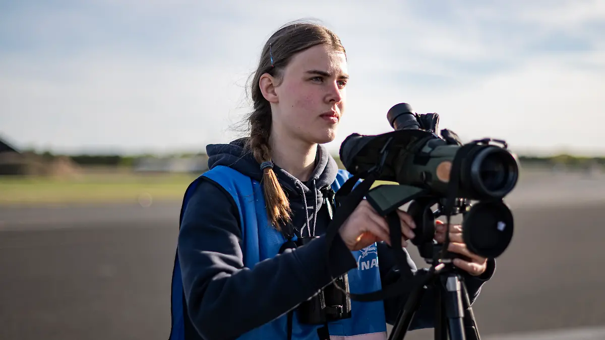 Cora Köberle, Mitglied des Young Birders Club, beobachtet auf dem Flugfeld des stillgelegten Flughafen Tegel mit einem Fernglas Vögel. (zu dpa: «Fernglas statt Handy: Warum die Gen Z jetzt Birden geht») +++ dpa-Bildfunk +++