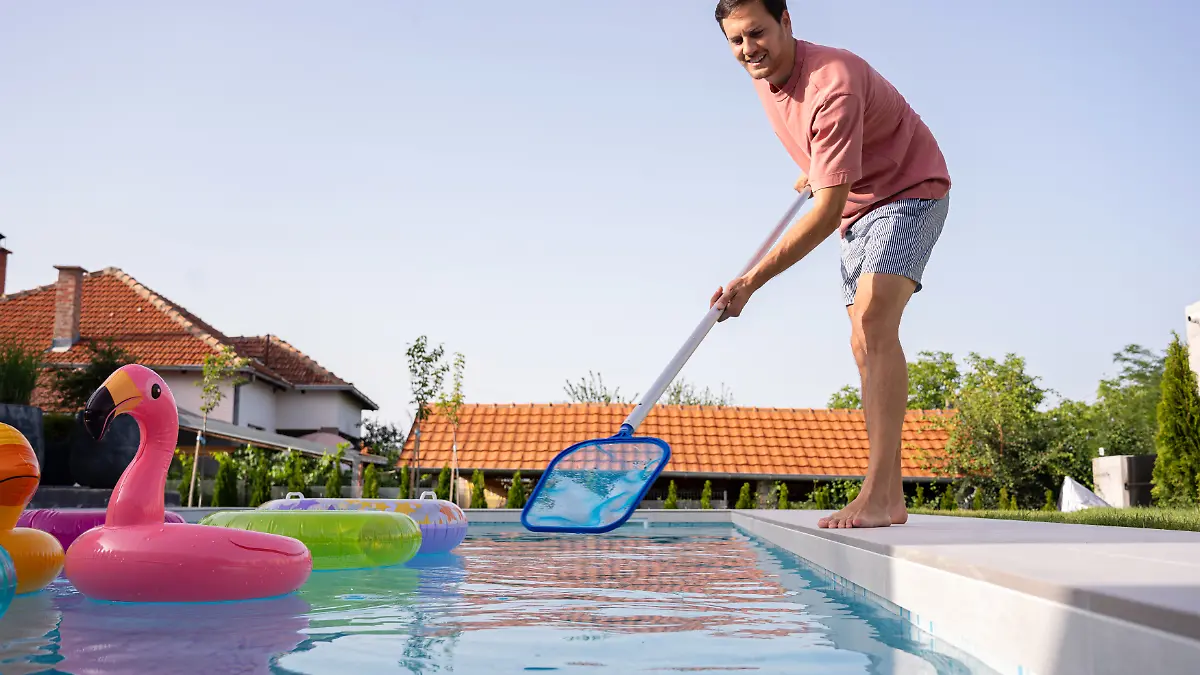 Ein junger Mann reinigt seinen Swimmingpool im Hinterhof mit einem Netz.
