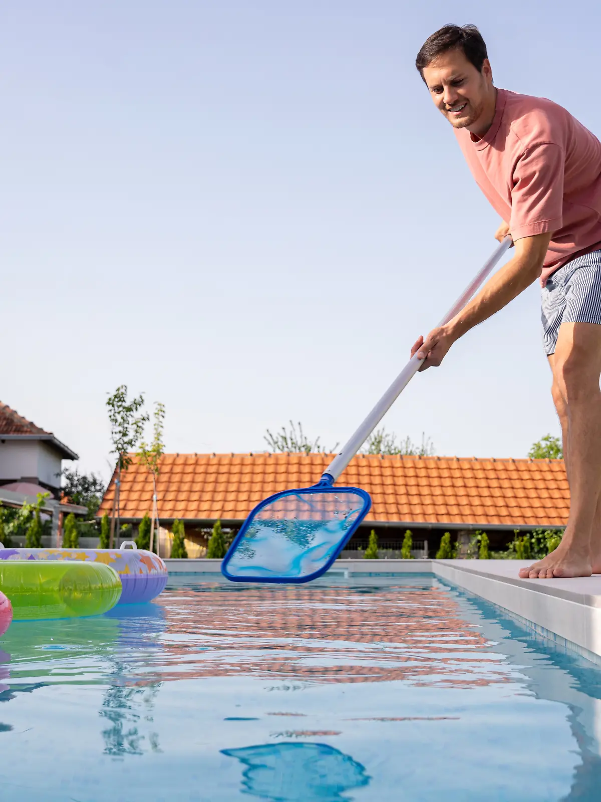 Ein junger Mann reinigt seinen Swimmingpool im Hinterhof mit einem Netz.