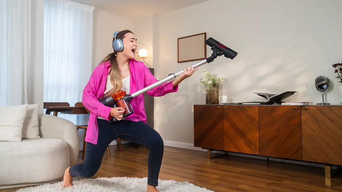Frau singt mit einem kabellosen Staubsauger in einem modernen Wohnzimmer.