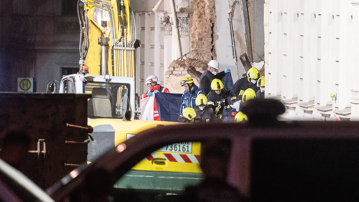 Hinter einem Sichtschutz tragen die Einsatzkräfte der Feuerwehr eine Leiche aus den Trümmern.