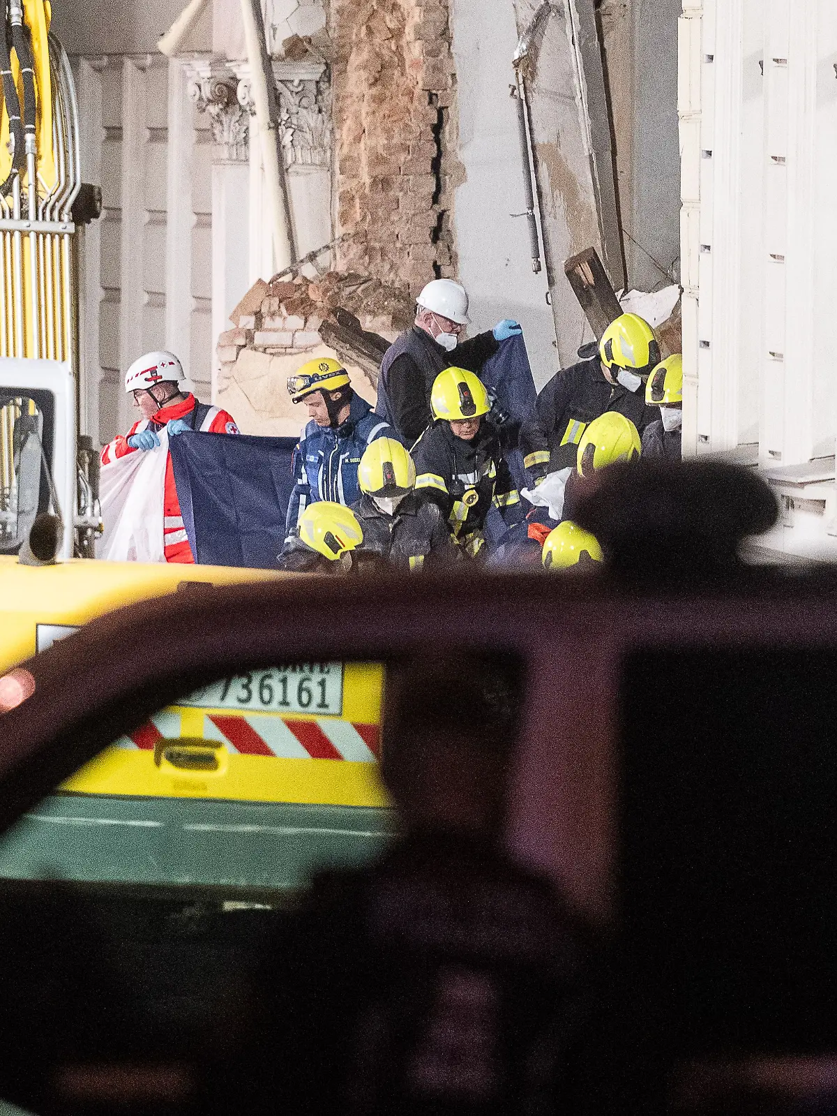 Hinter einem Sichtschutz tragen die Einsatzkräfte der Feuerwehr eine Leiche aus den Trümmern.