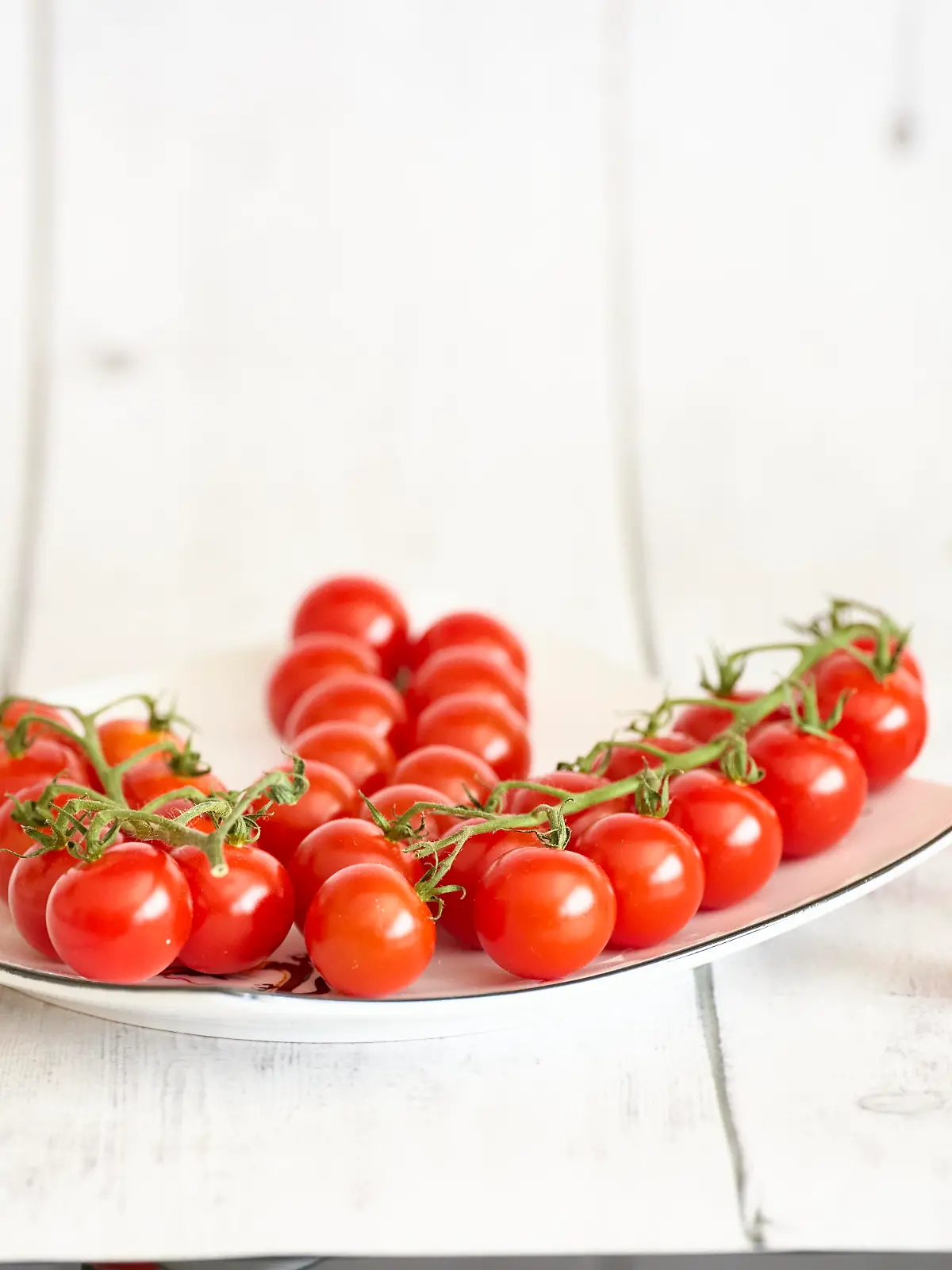 Rote Cherrytomaten auf weissem Teller und weissem Holztisch. Fehraltorf, Schweiz