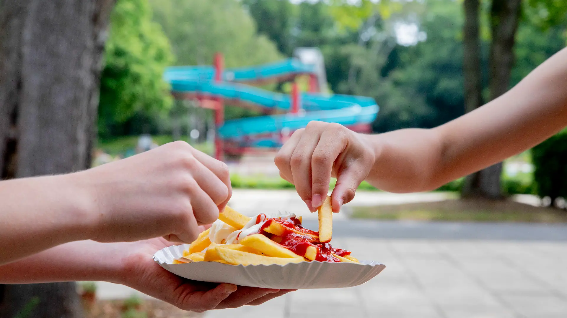 18.06.2020, Berlin: Kinder essen im Sommerbad Humboldthain Pommes mit Ketchup und Mayo vom Imbiss «Tropez». (zu dpa "Pommes: Warum kriegt man im Freibad Heißhunger drauf?") Foto: Christoph Soeder/dpa +++ dpa-Bildfunk +++