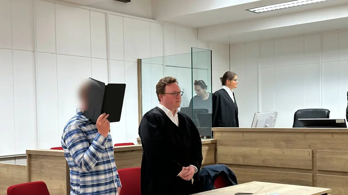 Der Angeklagte verdeckt sein Gesicht mit einem Ordner.