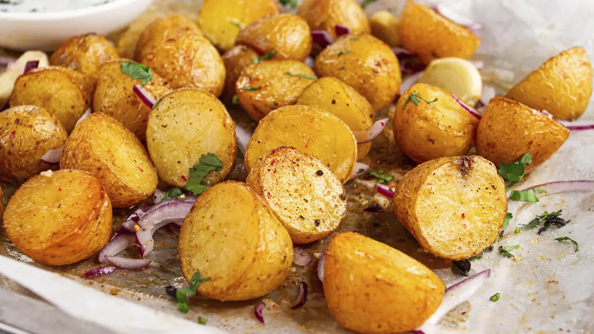 Bratkartoffeln liegen auf einem Backblech neben gehackten Kräutern und roten...