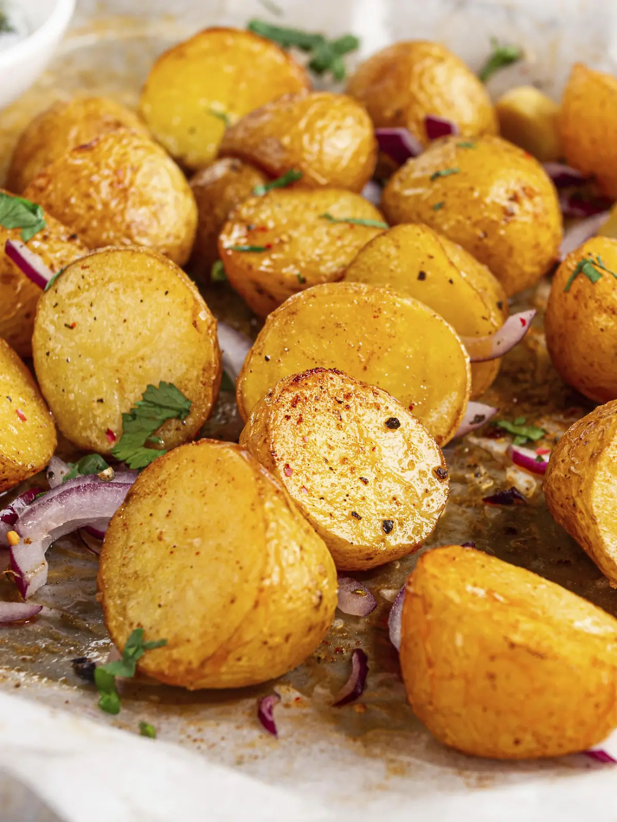 Bratkartoffeln liegen auf einem Backblech neben gehackten Kräutern und roten...