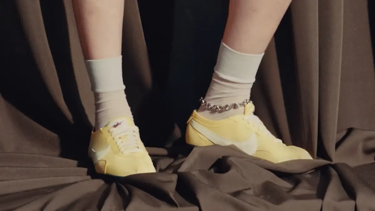 Nike Moon Shoe Original in Butter Yellow an den Füßen eines Models vor dunklem Hintergrund.