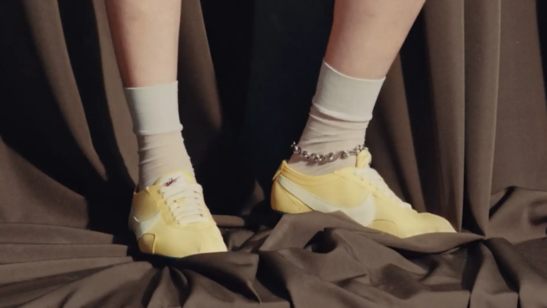 Nike Moon Shoe Original in Butter Yellow an den Füßen eines Models vor dunklem Hintergrund.