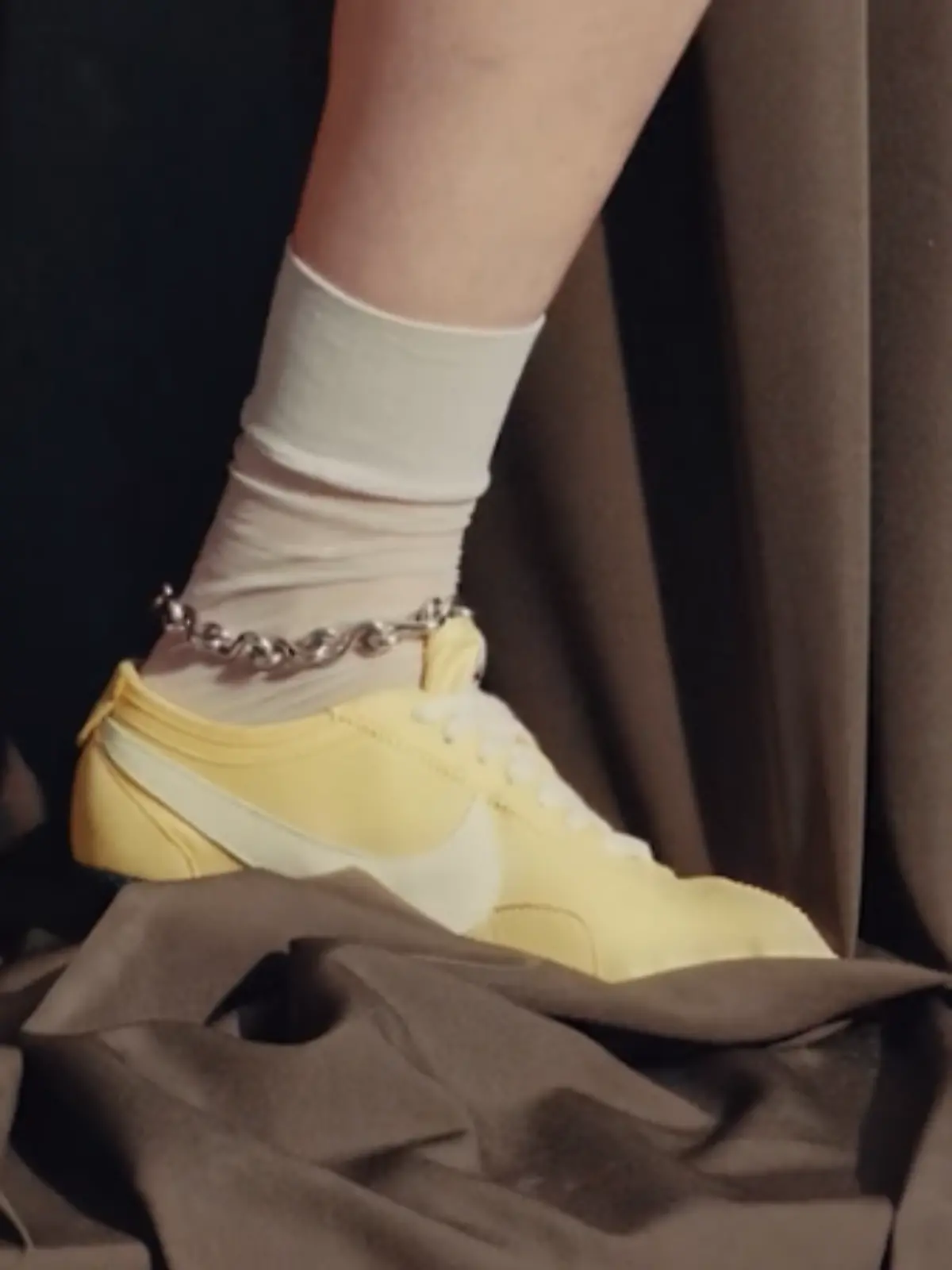 Nike Moon Shoe Original in Butter Yellow an den Füßen eines Models vor dunklem Hintergrund.