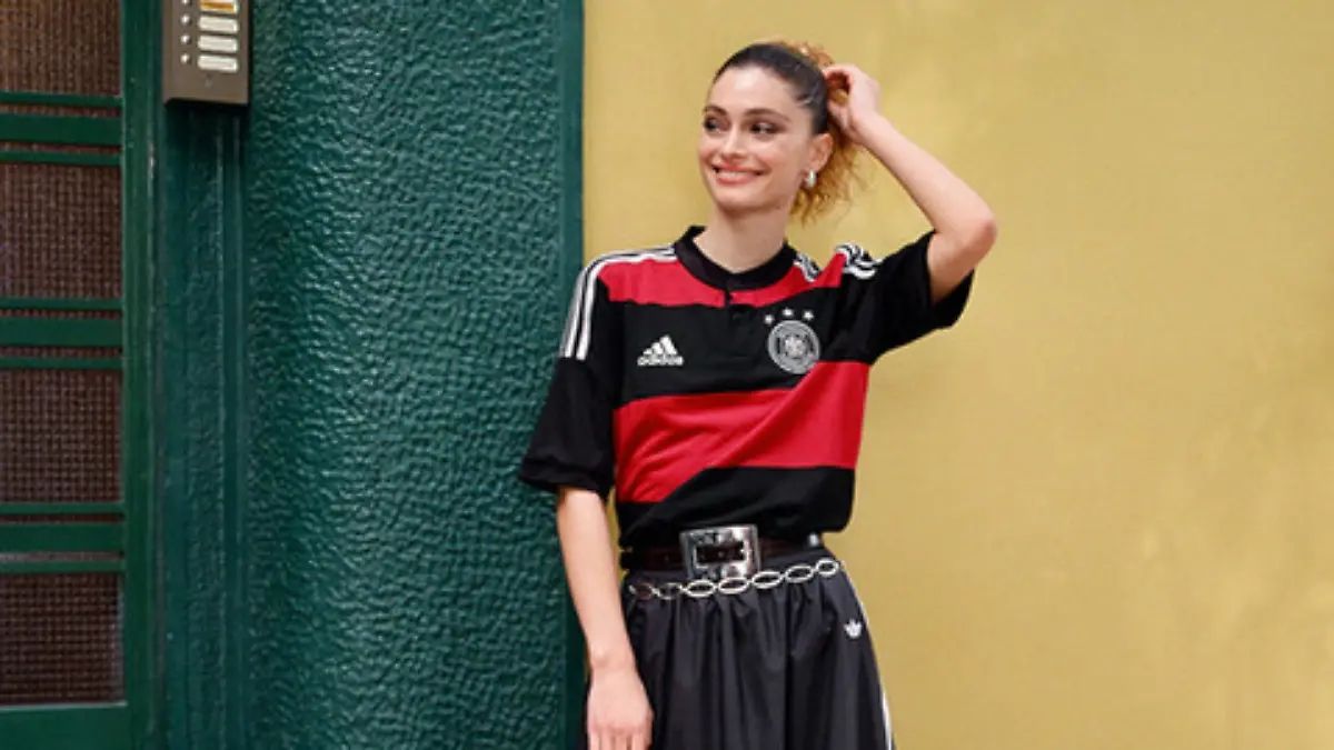 Model in einem Adidas-Look mit DFB-Trikot vor einer Hauswand.