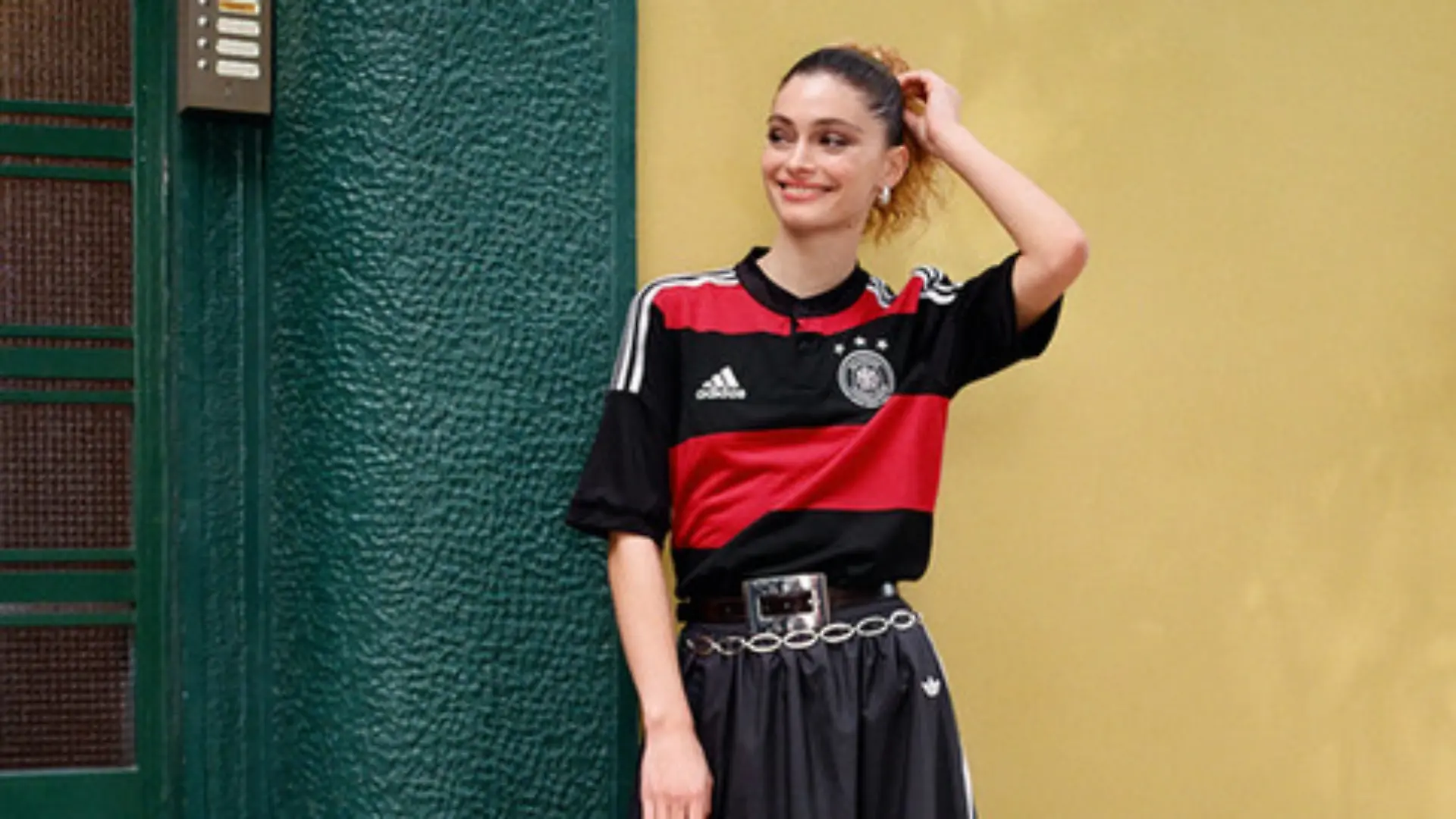 Model in einem Adidas-Look mit DFB-Trikot vor einer Hauswand.