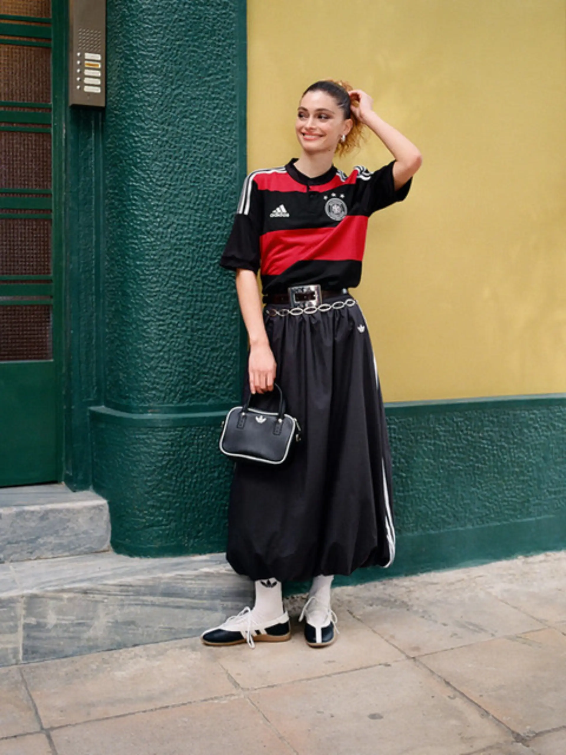 Model in einem Adidas-Look mit DFB-Trikot vor einer Hauswand.