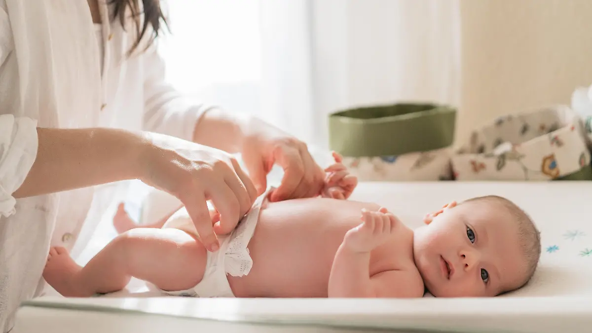 Baby wird auf dem Wickeltisch von einer Frau gewickelt.