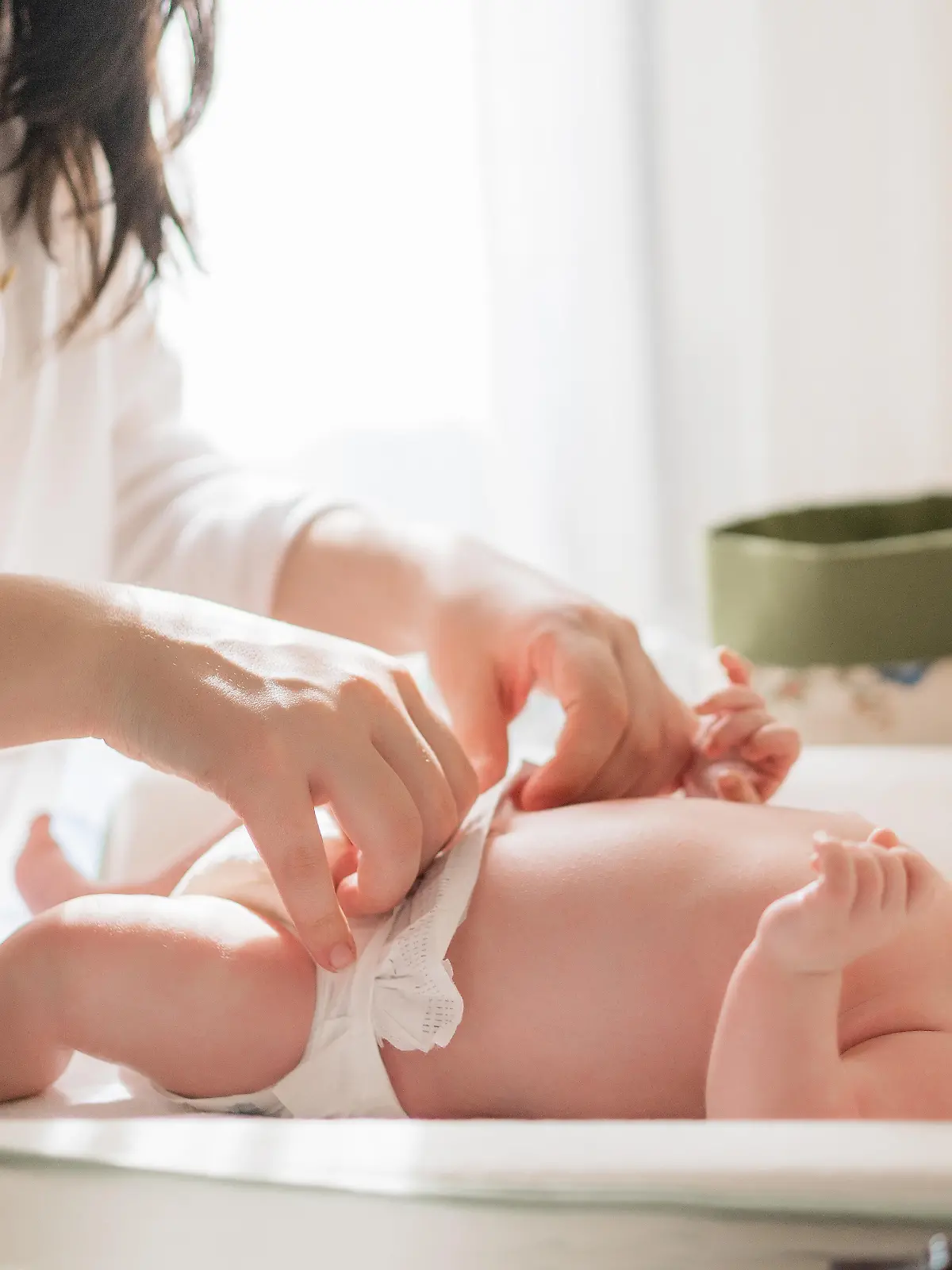 Baby wird auf dem Wickeltisch von einer Frau gewickelt.
