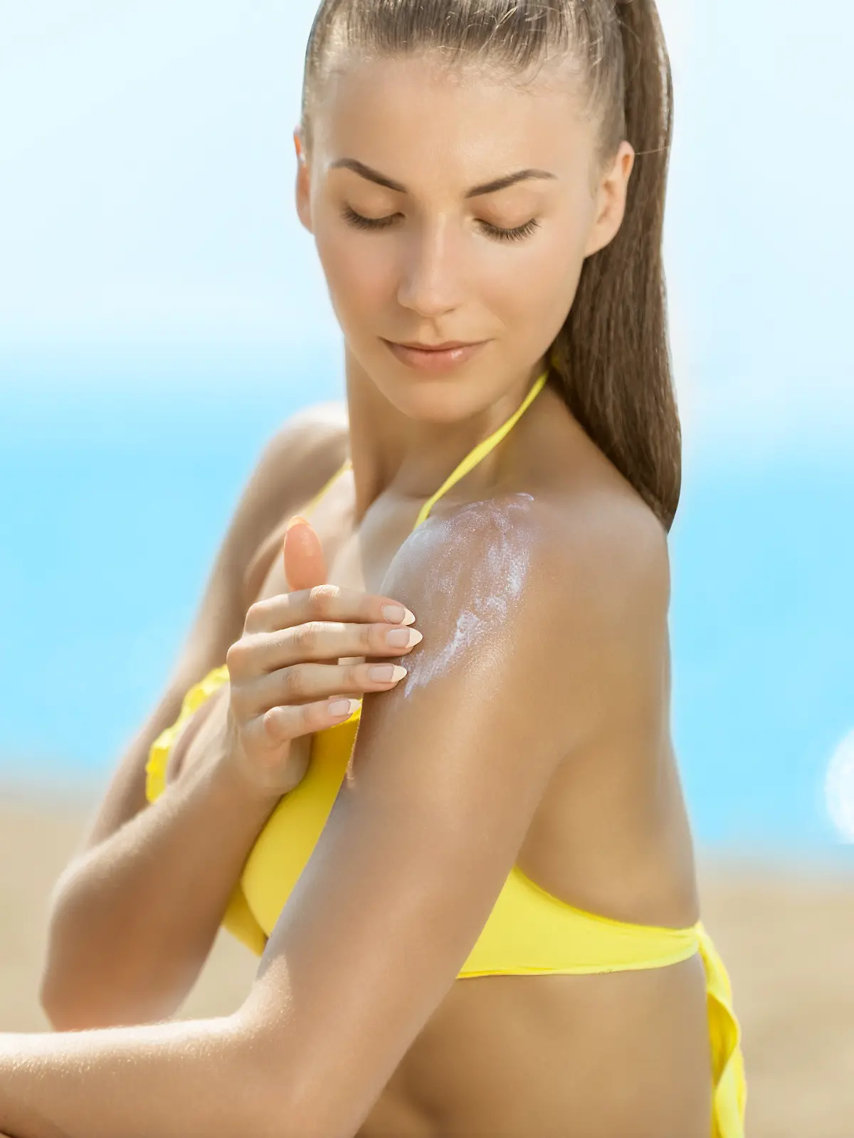 Frau im gelben Bikini cremt sich ein.