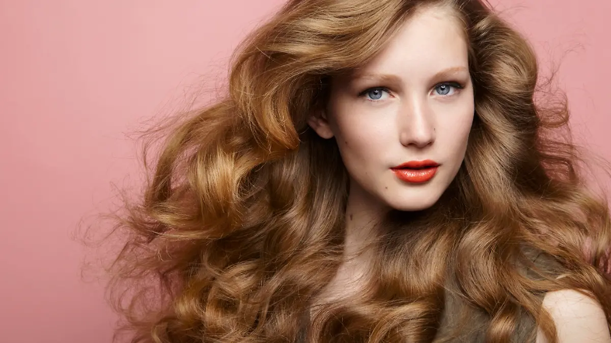 Ein Beauty-Foto einer Brünetten mit professioneller Frisur und Make-up vor einem dunklen Hintergrund