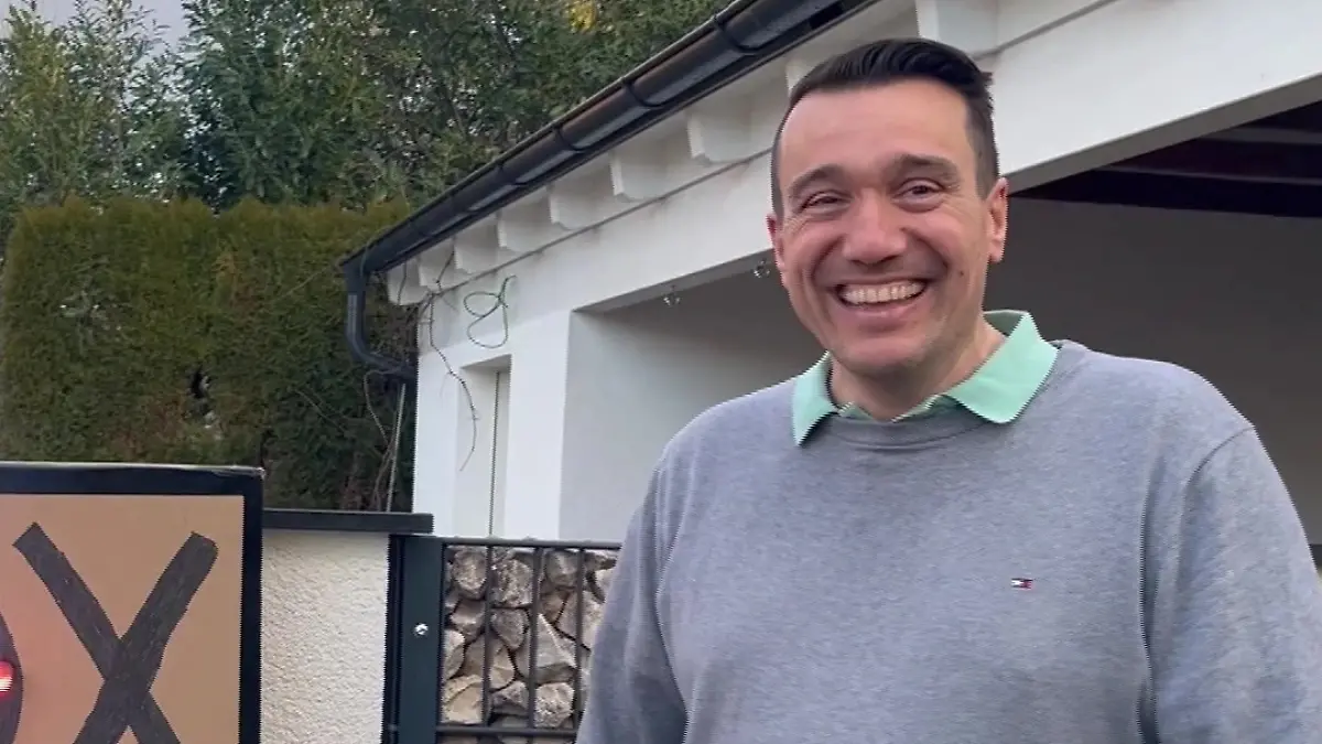 Freddy steht lachend vor einer Garage.