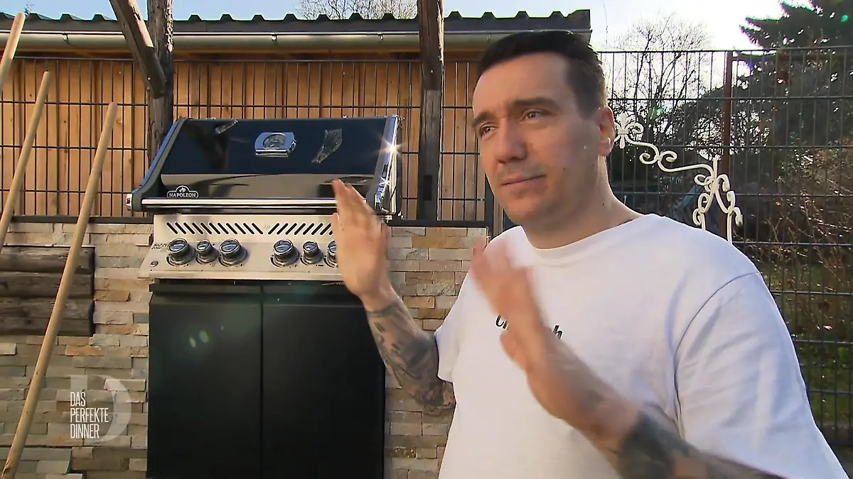 Freddy steht gestikulierend vor einem Grill.