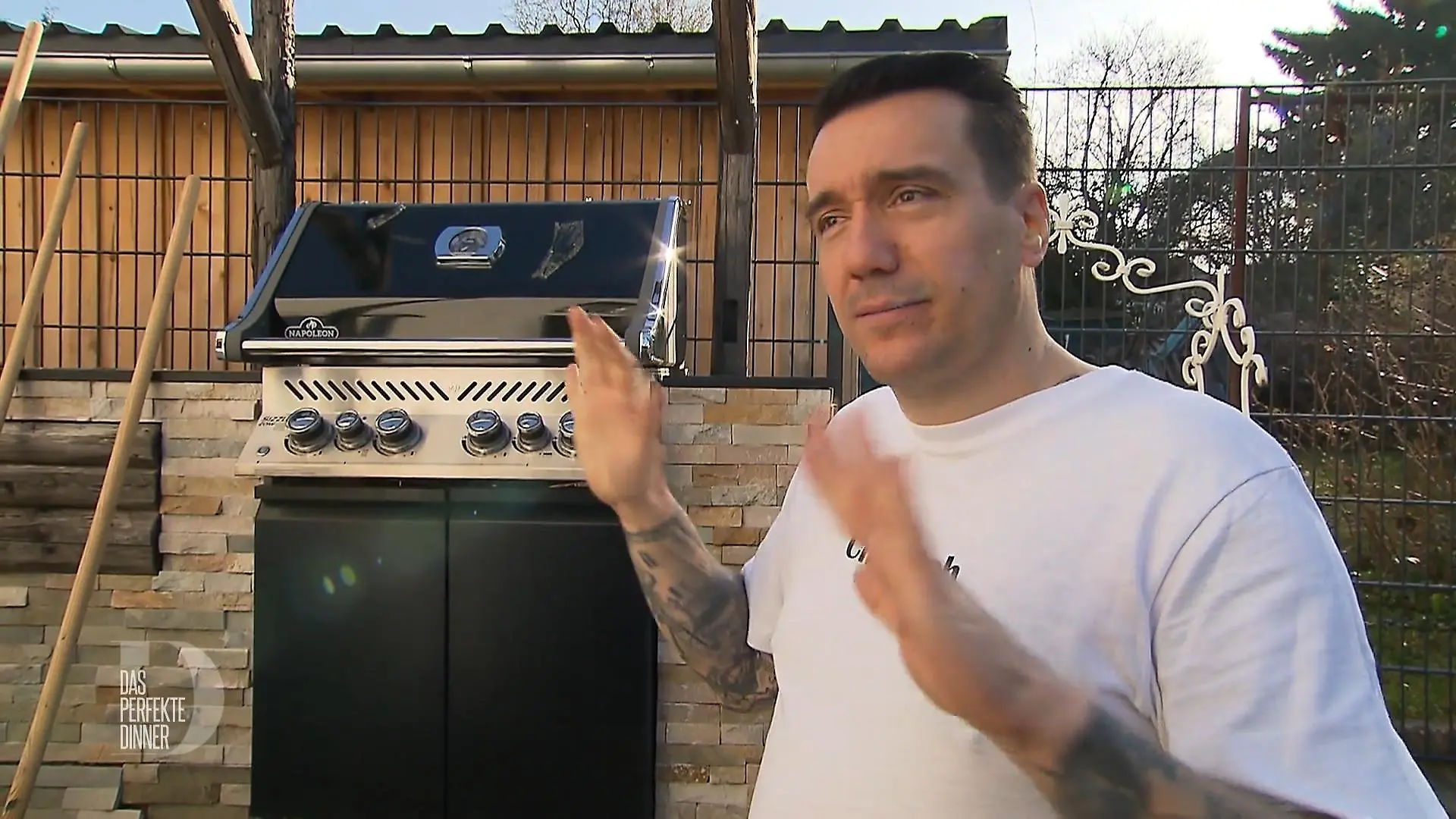 Freddy steht gestikulierend vor einem Grill.