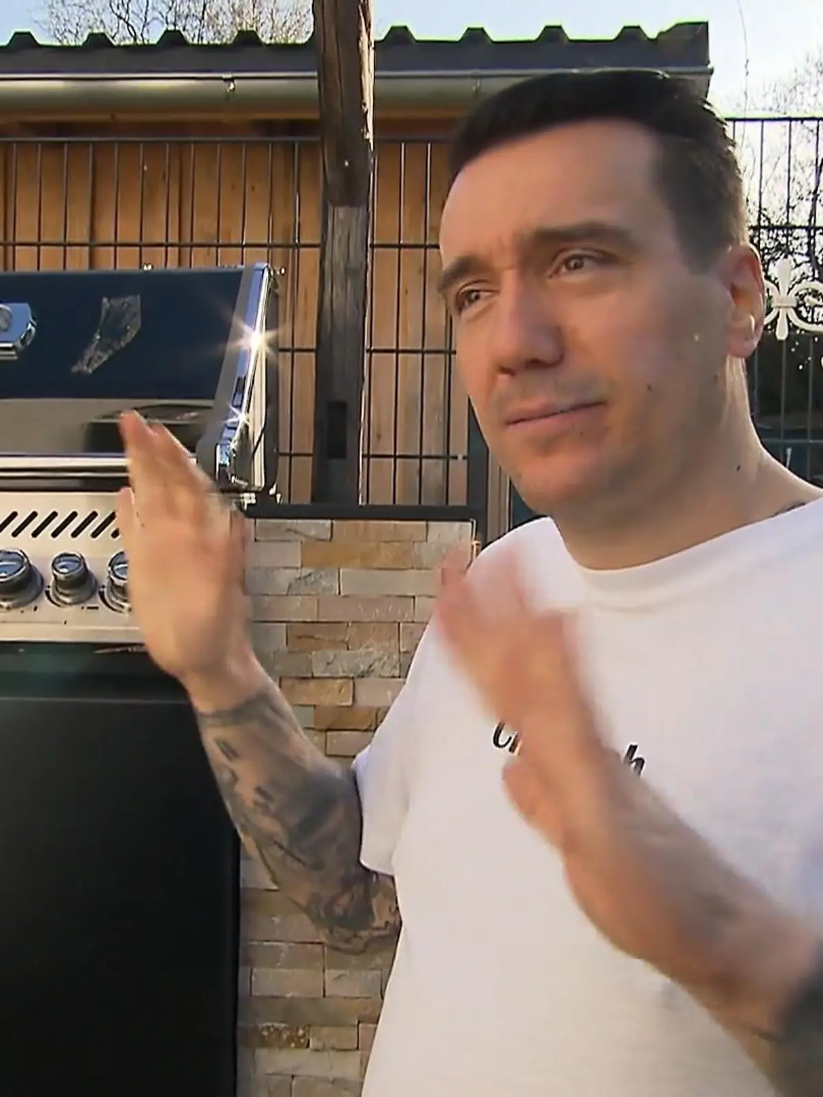 Freddy steht gestikulierend vor einem Grill.
