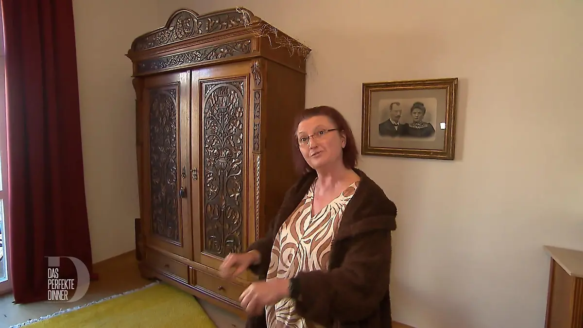 Katja steht vor einem schmuckvoll verzierten Holzschrank.