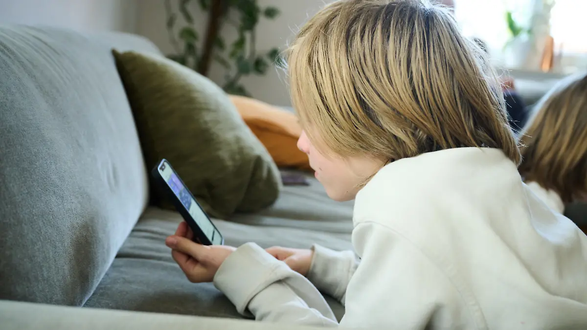 ARCHIV - 21.04.2025, Bayern, Roth: Ein Junge liegt auf einem Sofa und blickt auf sein Smartphone. (gestellte Szene). (zu dpa: «Mobbing, Pornos, Gewaltvideos - Was geht ab im Klassenchat?») Foto: Annette Riedl/dpa +++ dpa-Bildfunk +++