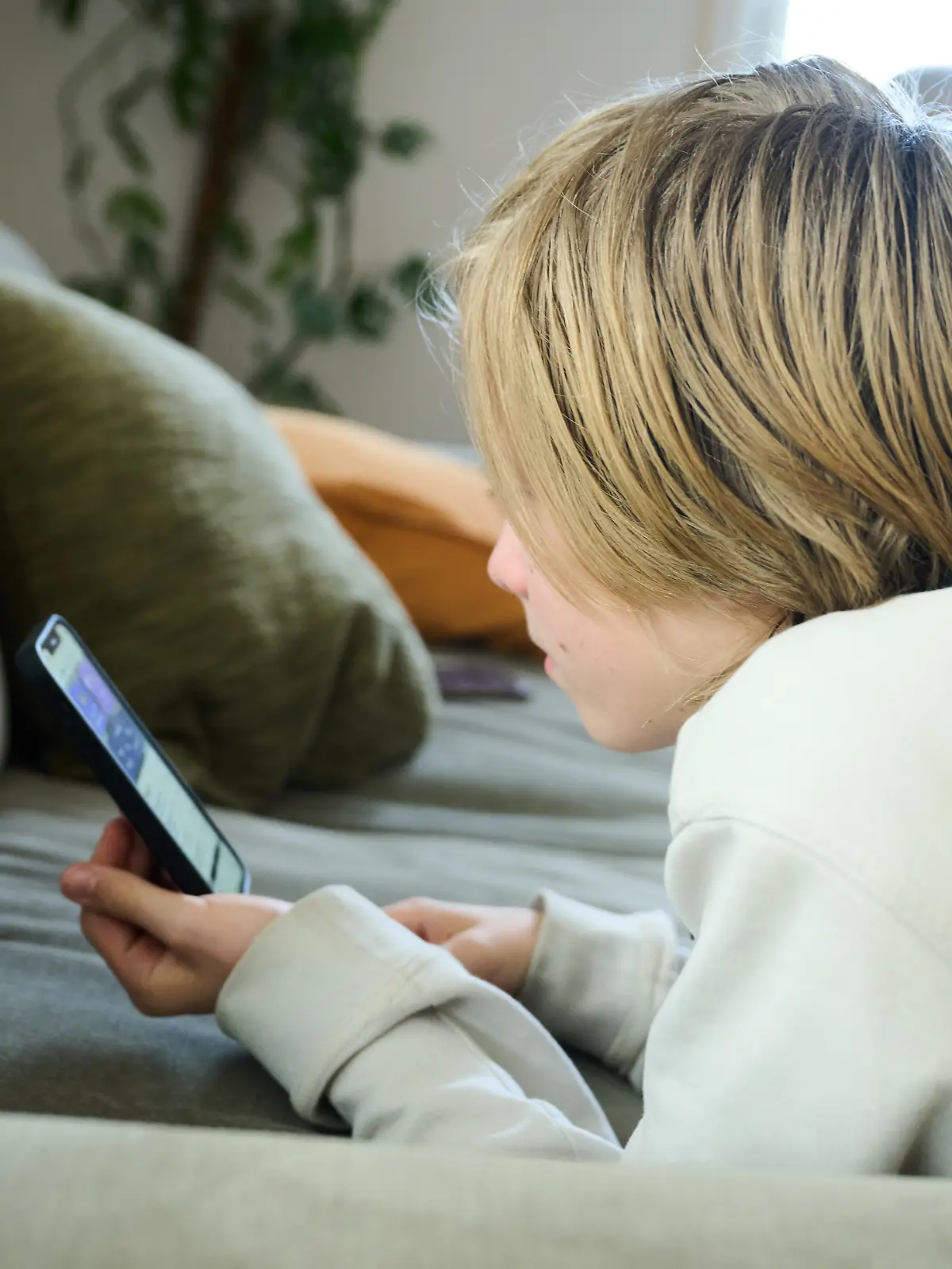 ARCHIV - 21.04.2025, Bayern, Roth: Ein Junge liegt auf einem Sofa und blickt auf sein Smartphone. (gestellte Szene). (zu dpa: «Mobbing, Pornos, Gewaltvideos - Was geht ab im Klassenchat?») Foto: Annette Riedl/dpa +++ dpa-Bildfunk +++