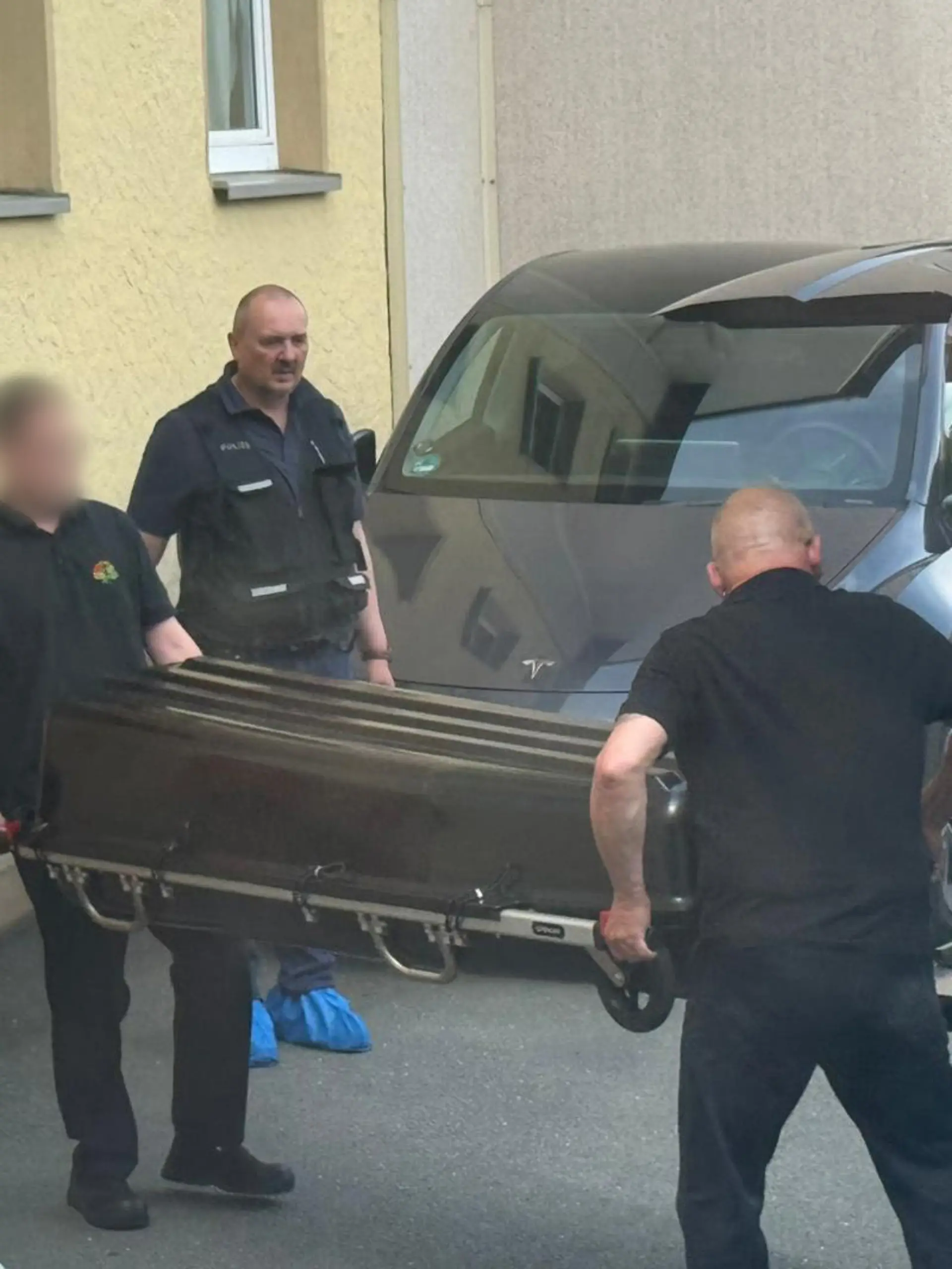 31.05.2026, Bayern, Konradsreuth: Mitarbeiter eines Bestattungsunternehmens tragen einen Sarg aus einem Mehrfamilienhaus. In einer Wohnung im bayerischen Konradsreuth (Landkreis Hof) ist ein Toter gefunden worden. Die Polizei geht von einer Gewalttat aus. Foto: N5 DESK/NEWS5/dpa - ACHTUNG: Mitarbeiter des Bestattungsunternehmens aus rechtlichen Gründen gepixelt +++ dpa-Bildfunk +++