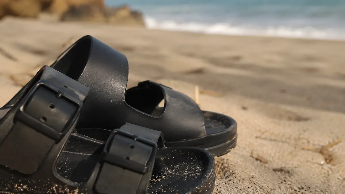 Pantoletten in Schwarz am Strand.