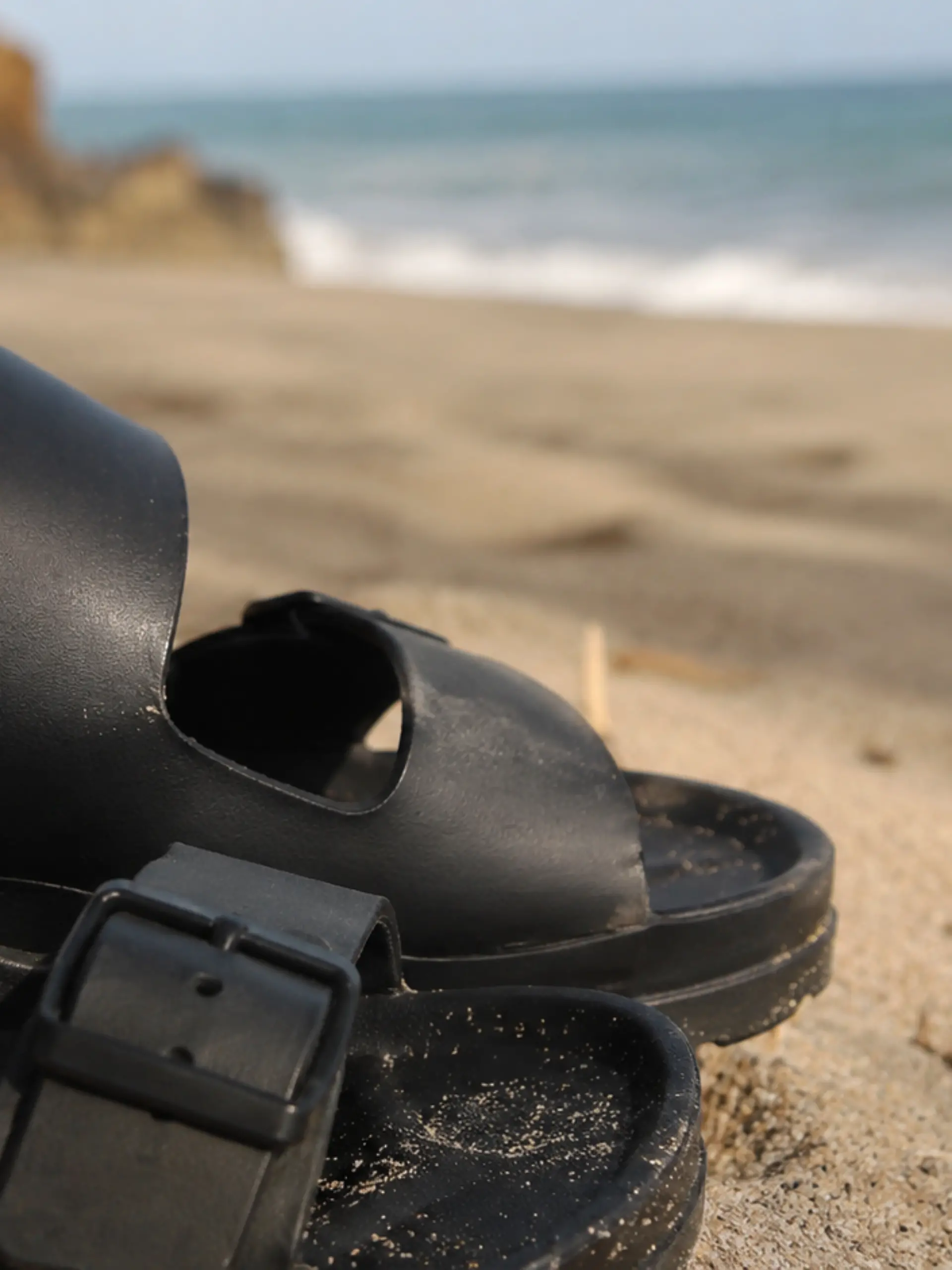 Pantoletten in Schwarz am Strand.