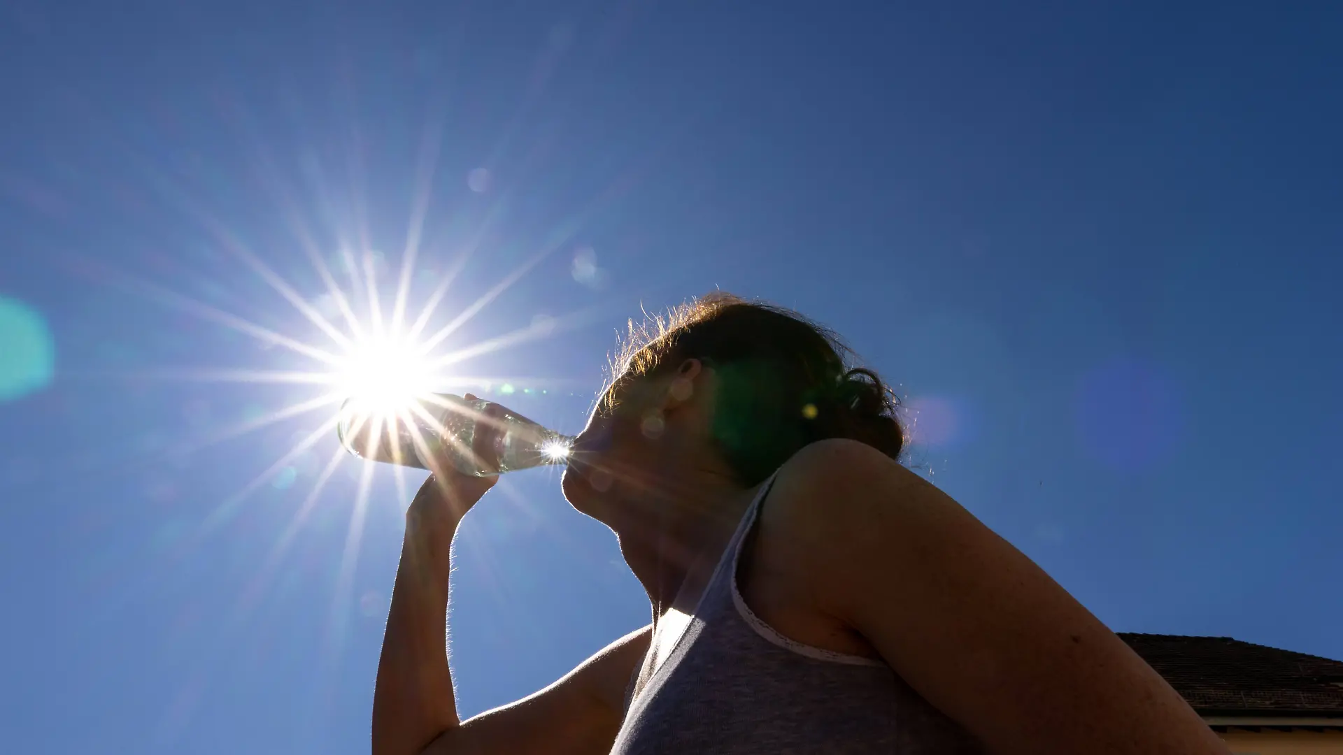 Hitzewelle in Deutschland Illustration - Eine Frau trinkt vor dem blauem Himmel mit der Sonne Wasser aus einer Flasche., Oberursel Hessen Deutschland