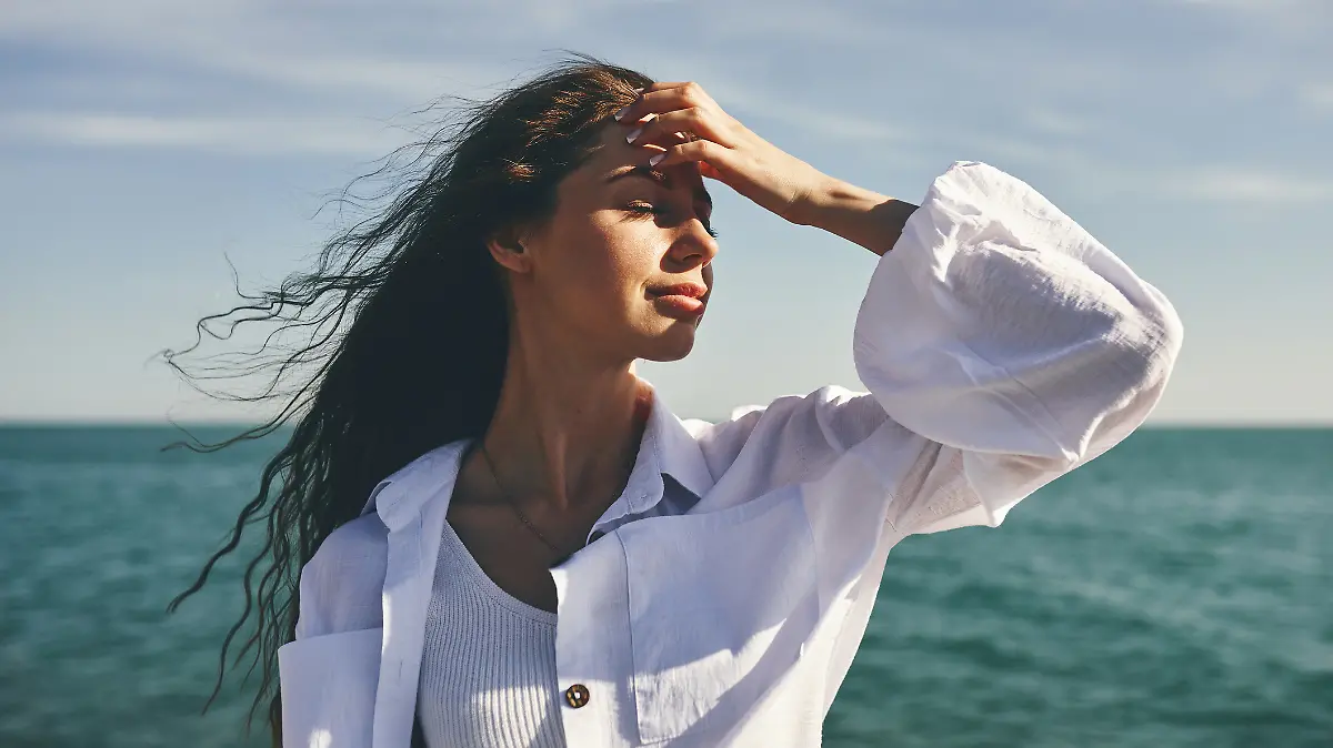Eine Frau mit Beach Waves steht mit dem Rücken zum Meer.
