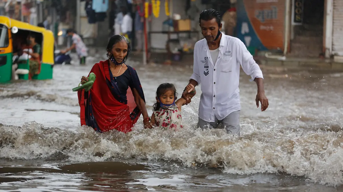 22.06.2021, Indien, Ahmedabad: Menschen gehen durch eine überflutete Straße nach starken Regenfällen. Foto: Ajit Solanki/AP/dpa +++ dpa-Bildfunk +++