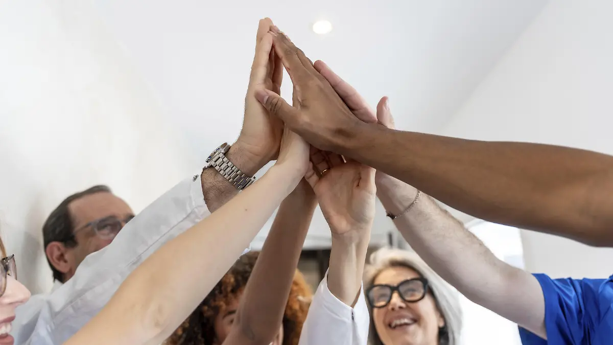 Angehörige der Gesundheitsberufe mit unterschiedlichem Hintergrund feiern Erfolg und Teamwork und heben begeistert ihre Hände in einem High Five als Symbol für Einheit und Leistung in der Medizin || Modellfreigabe vorhanden