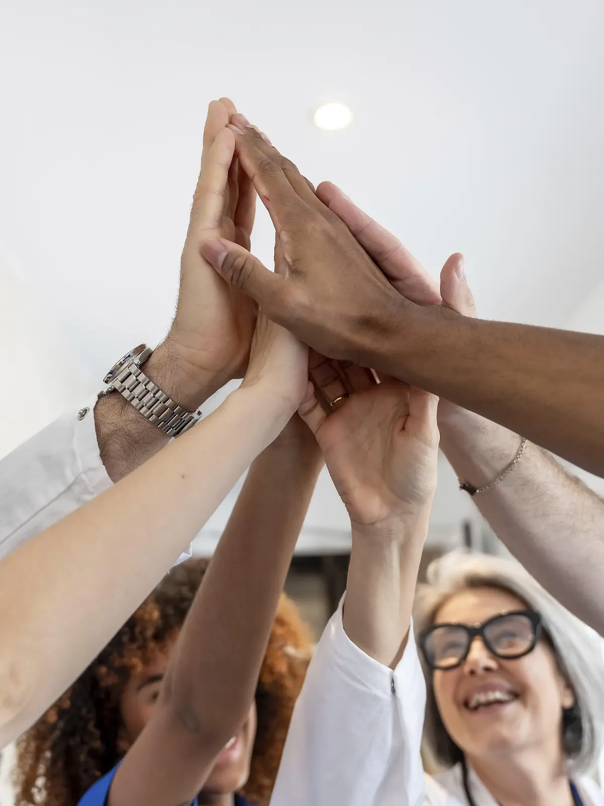 Angehörige der Gesundheitsberufe mit unterschiedlichem Hintergrund feiern Erfolg und Teamwork und heben begeistert ihre Hände in einem High Five als Symbol für Einheit und Leistung in der Medizin || Modellfreigabe vorhanden