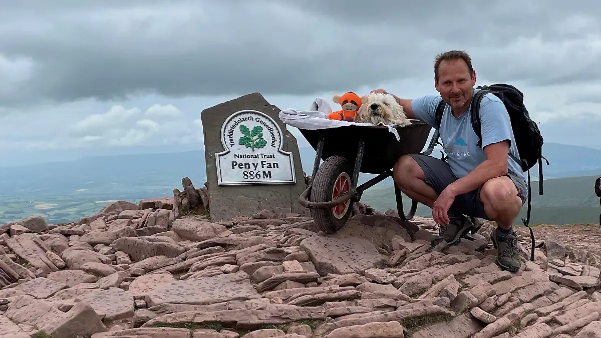 Herrchen Carlos und Hund Monty posieren vor dem Schild des Berges Pen y Fan.