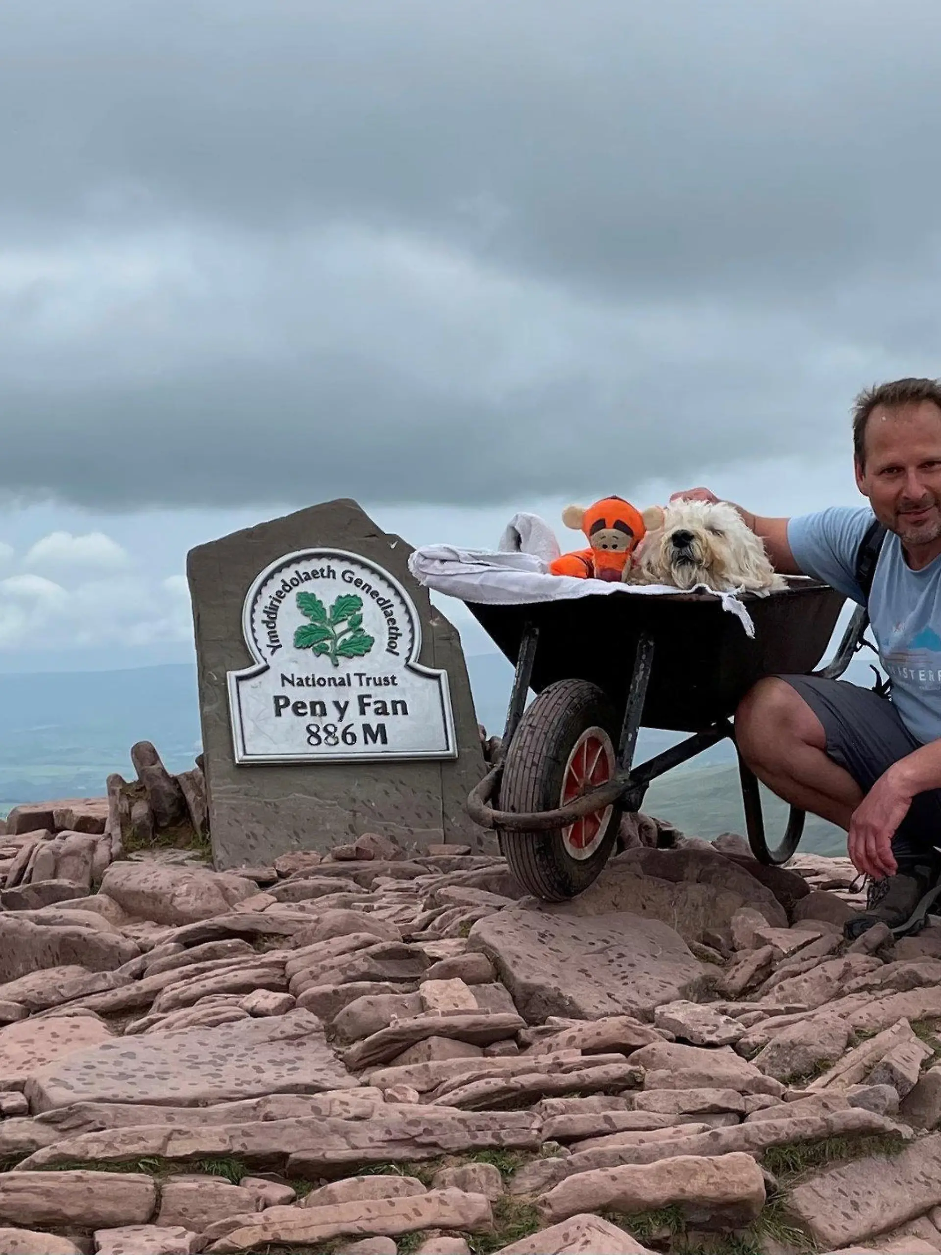 Herrchen Carlos und Hund Monty posieren vor dem Schild des Berges Pen y Fan.