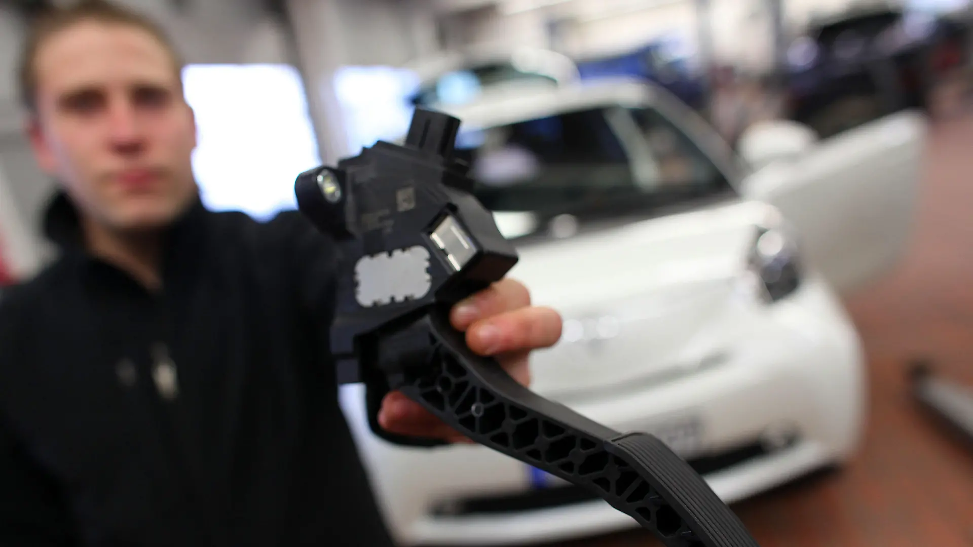 Ein Mechaniker zeigt am Donnerstag (04.02.2010) in der Werkstatt der Toyota-Zentrale in Köln vor einem Toyota iQ ein Gaspedal, wie es in den vom Rückruf betrofenen Fahrzeugen eingebaut ist. Vom Toyota-Rückruf wegen klemmender Gaspedale sind in Deutschland 215 796 Autos betroffen. Betroffen sind unterschiedliche Baujahre der Modelle AYGO, iQ, Yaris, Auris, Corolla, Verso, Avensis und RAV4. Foto: Oliver Berg dpa/lnw (zu dpa 0219) +++(c) dpa - Bildfunk+++