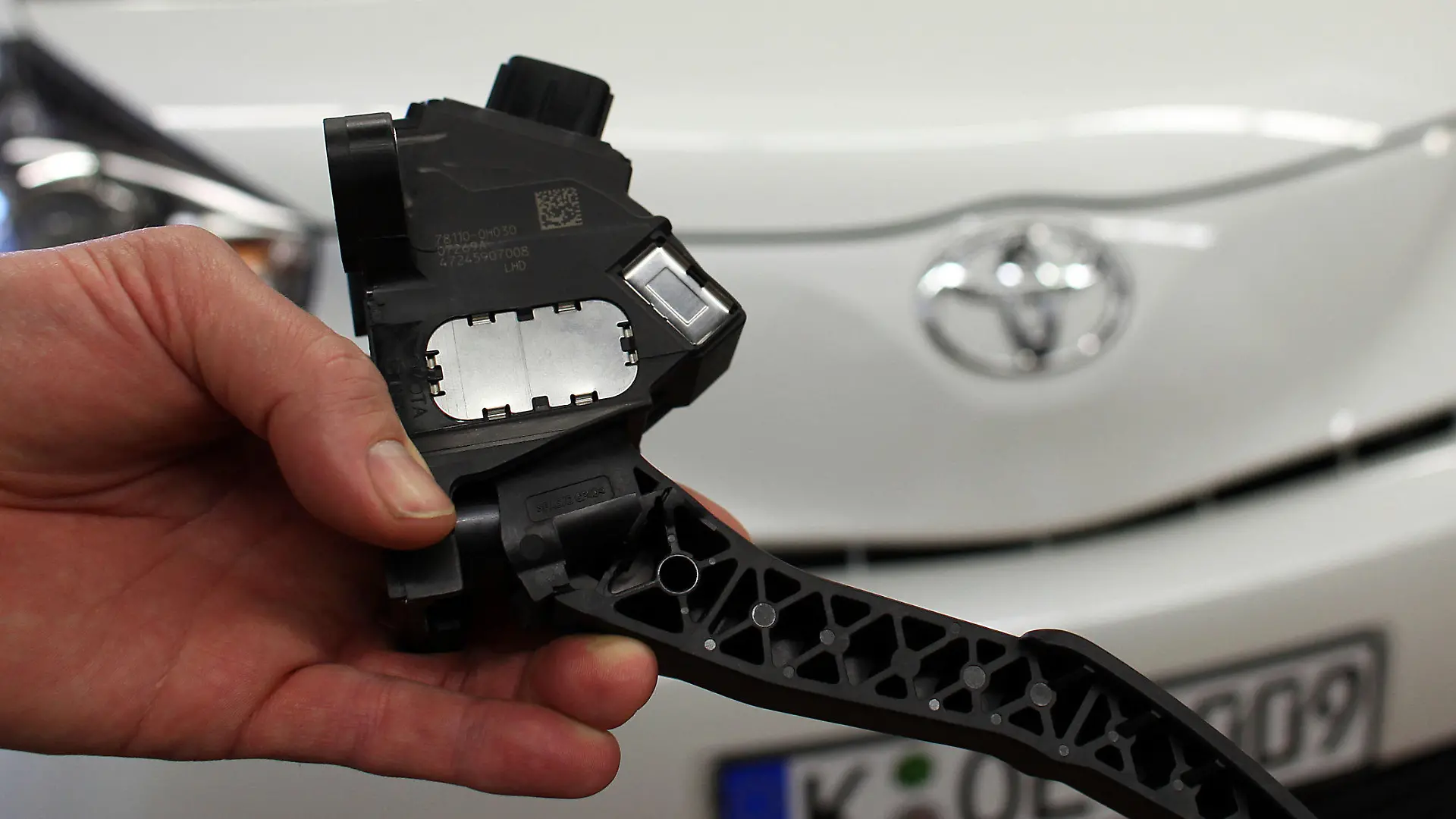 Ein Mechaniker zeigt am Donnerstag (04.02.2010) in der Werkstatt der Toyota-Zentrale in Köln vor einem Toyota iQ ein Gaspedal, wie es in den vom Rückruf betrofenen Fahrzeugen eingebaut ist. Vom Toyota-Rückruf wegen klemmender Gaspedale sind in Deutschland 215 796 Autos betroffen. Betroffen sind unterschiedliche Baujahre der Modelle AYGO, iQ, Yaris, Auris, Corolla, Verso, Avensis und RAV4. Foto: Oliver Berg dpa/lnw (zu dpa 0219) +++(c) dpa - Bildfunk+++