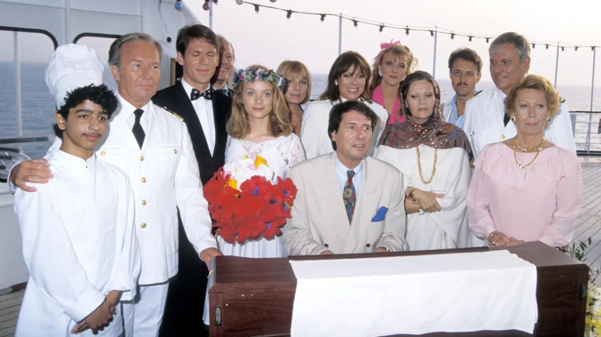 Baris Cetinkeya, Horst Neumann, Tobias Hoesl Tushka Bergen, Herbert Tennigkeit, Karyn von Ostholt, Heide Keller, Nicole Belstler-Boettcher, Louise Martini, Peter Kennigkeit, Heinz Weiss, Heli Finkenzeller (v.l.n.r.), Udo Jürgens (Sänger m.), Dreharbeiten zur ZDF-Reihe "Traumschiff", Folge 18: "Florida", MS "Berlin", Kreuzfahrt, Kreuzfahrtschiff, Schiff, 20.03.1990, Hochzeit, Blumenstrauss, Blumen, Klavier, spielen, Flügel, Schauspieler, Schauspielerin, Promis, Prominente, Prominenter, (Photo by Peter Bischoff/Getty Images)