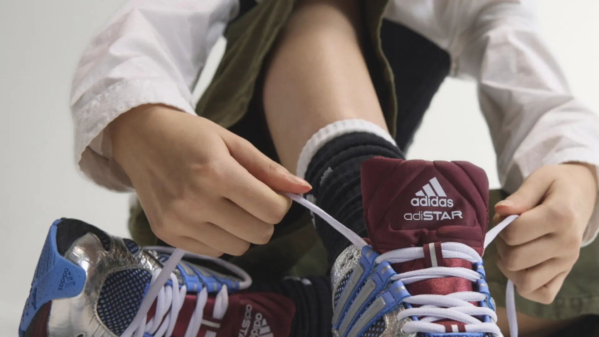 Model schnürt Adidas Adistar in Bordeaux, Blau und Silber zu.