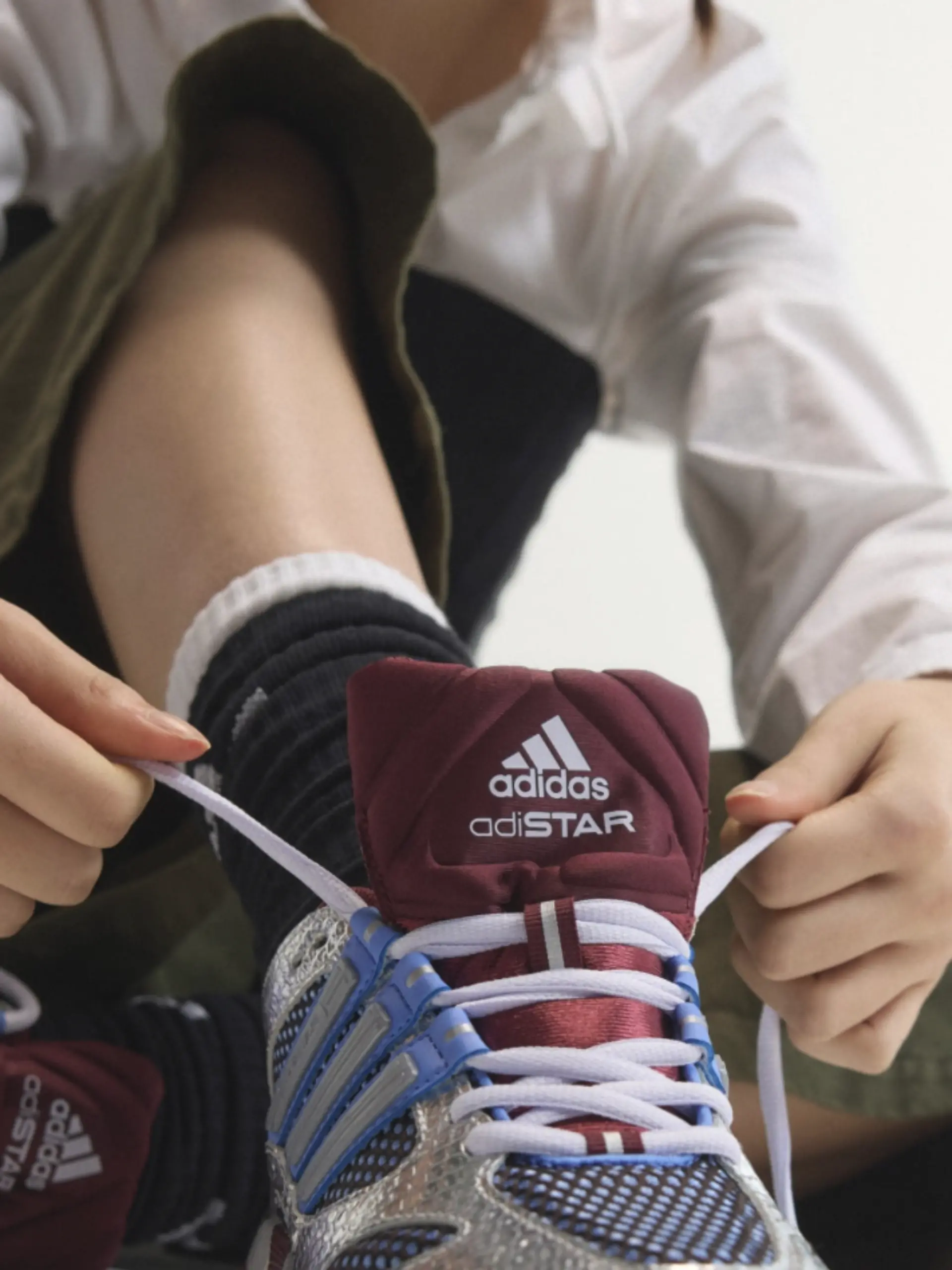 Model schnürt Adidas Adistar in Bordeaux, Blau und Silber zu.