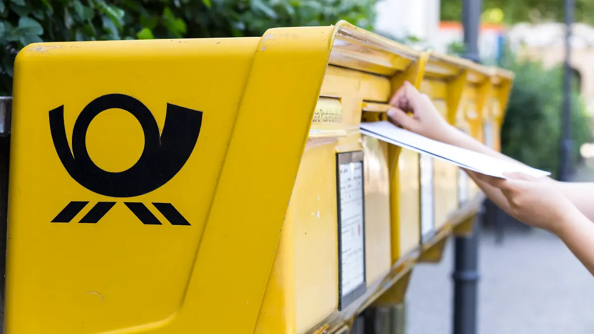 Mehrere Briefe werden in einen Briefkasten gesteckt. 