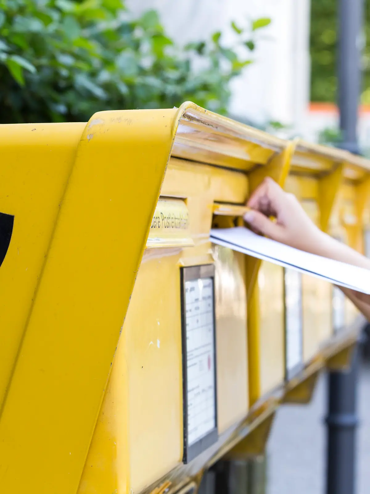 Mehrere Briefe werden in einen Briefkasten gesteckt.